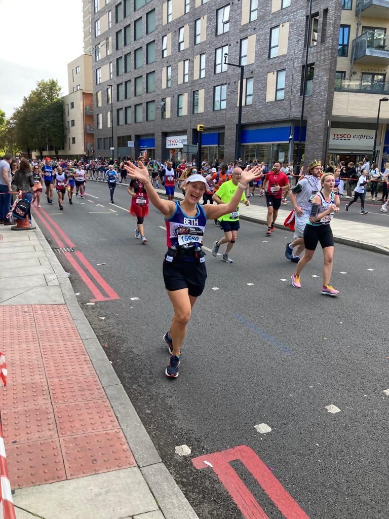A photo of Bethan, taking part way through her marathon run, shows Bethan running past the camera with her hands in the air and a big smile on her face