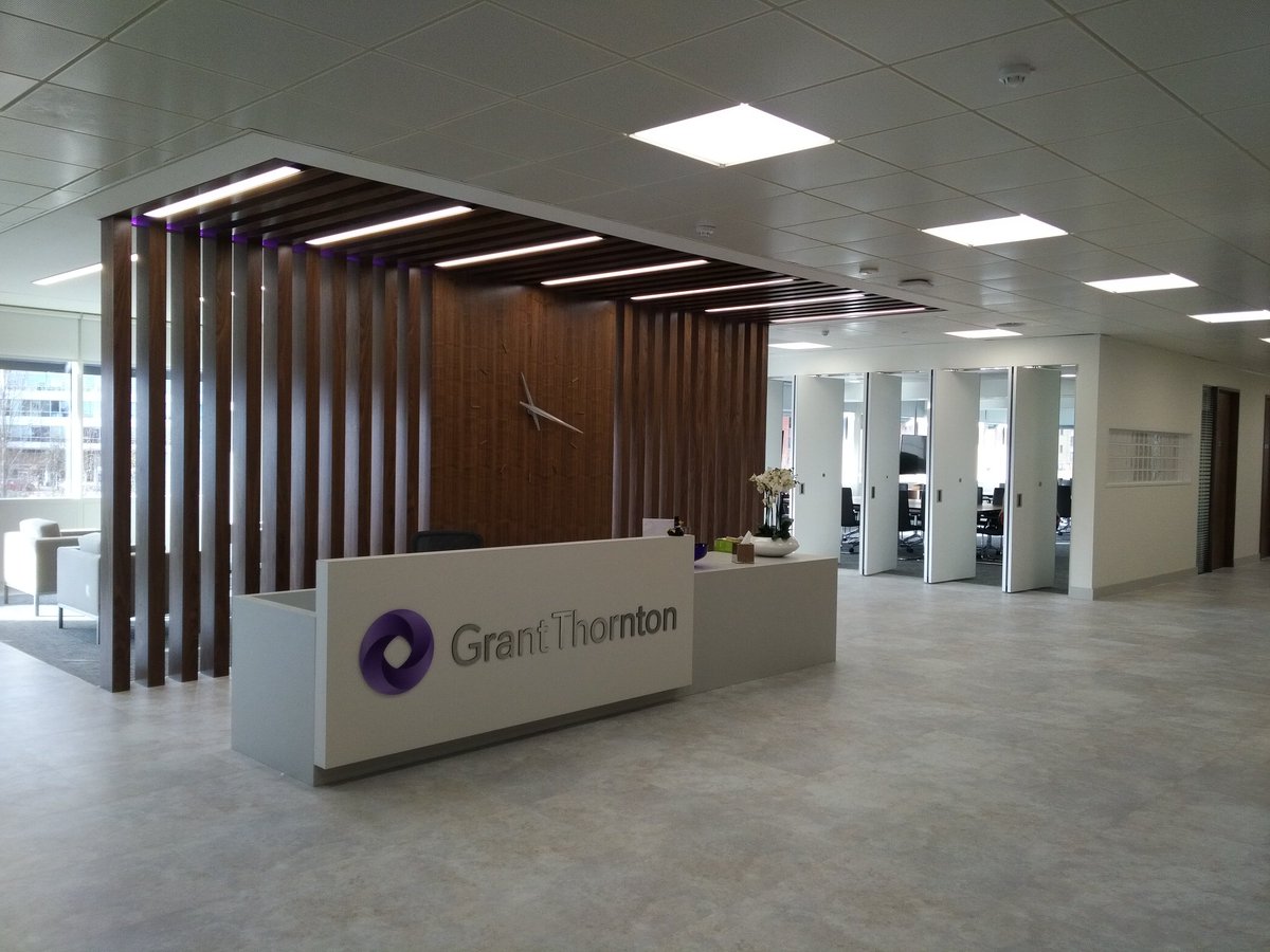 Photo shows the Bristol office reception, a large welcoming desk with the Grant Thornton logo on, in front of a wooden slat wall with the bright and open office space in the background